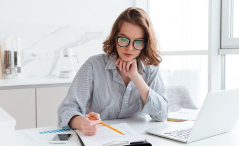 Photo d'une femme en train de remplir des documents administratifs relatifs aux taxes de construction pour une maison neuve.